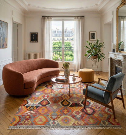 Tapis kilim Barak vintage de 65 ans aux motifs géométriques colorés, tissé à la main en Anatolie. Cette pièce d'artisanat d'exception sublime un salon de luxe à Paris, créant un contraste chic entre un canapé organique contemporain et le cachet d'un appartement ancien avec cheminée et parquet en chevrons.