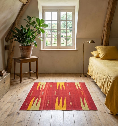Petit tapis kilim de Bodrum vintage (60 ans) aux tons rouge et jaune safran, tissé à la main en Anatolie. Disposé dans une chambre mansardée lumineuse avec parquet en bois clair, ce kilim artisanal apporte une touche bohème-chic et authentique à une décoration moderne et épurée.