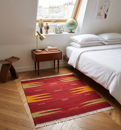 Petit tapis kilim de Bodrum vintage (60 ans) aux tons rouge et jaune safran, tissé à la main en Anatolie. Disposé dans une chambre parisienne avec parquet en bois clair, ce kilim artisanal apporte une touche bohème-chic et authentique à une décoration moderne et épurée.