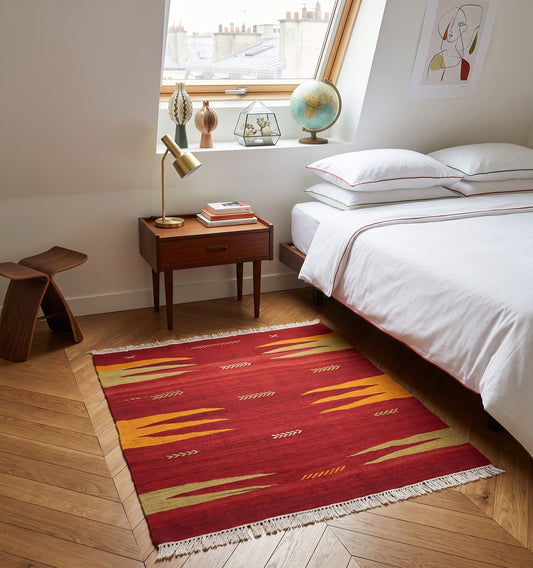 Petit tapis kilim de Bodrum vintage (60 ans) aux tons rouge et jaune safran, tissé à la main en Anatolie. Disposé dans une chambre parisienne avec parquet en bois clair, ce kilim artisanal apporte une touche bohème-chic et authentique à une décoration moderne et épurée.