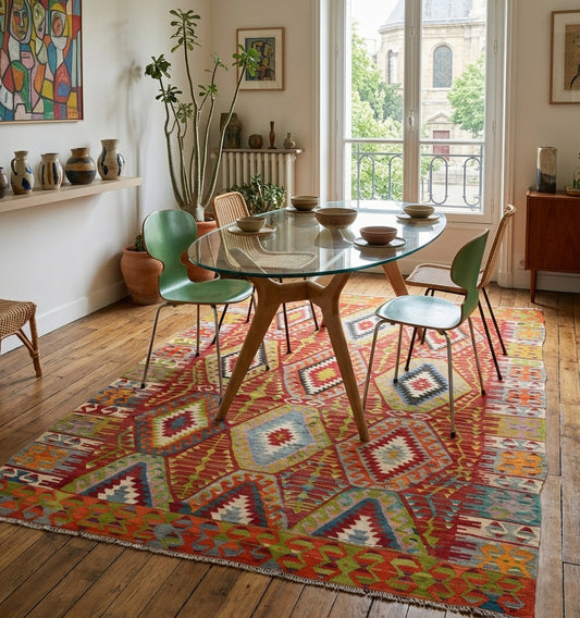 Grand tapis kilim Cal de 70 ans aux motifs losanges multicolores, tissé à la main en Anatolie. Cette pièce de collection artisanale délimite avec élégance l'espace salle à manger d'un appartement haussmannien à Paris, offrant un contraste vibrant entre l'artisanat ancien et un mobilier design des années 50.