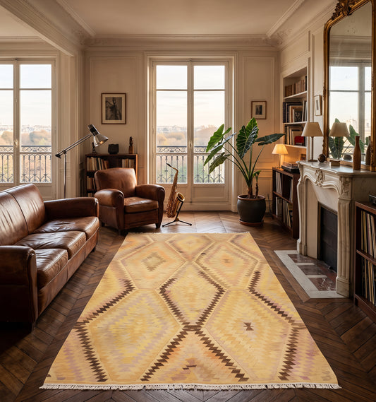 Tapis kilim tissé main aux losanges jaune safran et brun, tapis contemporain d'inspiration Anatolie posé sur parquet en chevrons dans un salon haussmannien parisien face à une cheminée en marbre
