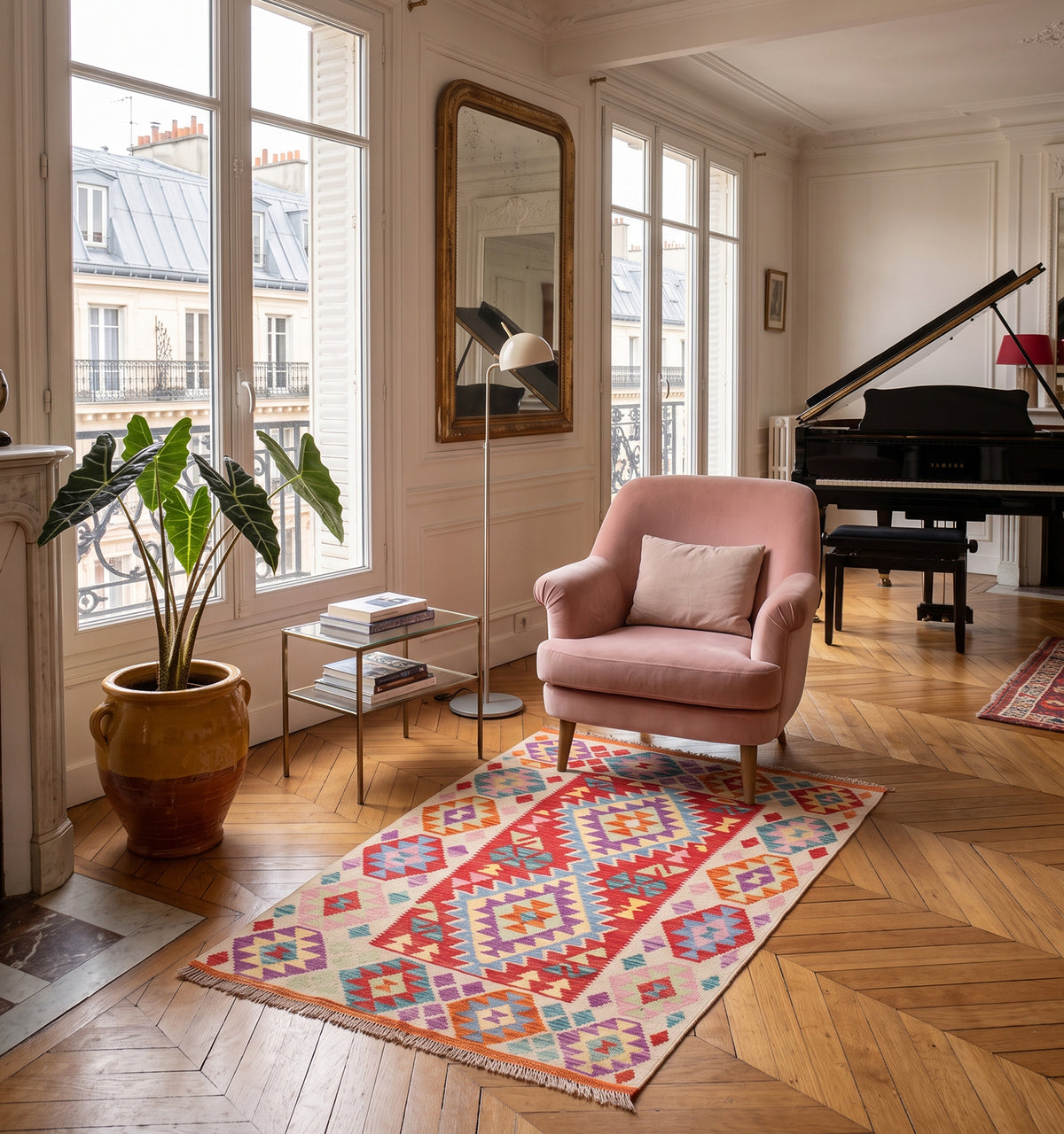 Tapis kilim tissé main aux losanges rouge, mauve et corail, tapis contemporain d’inspiration Anatolie posé sur parquet en chevrons dans un salon parisien face à un fauteuil rose poudré et un piano à queue