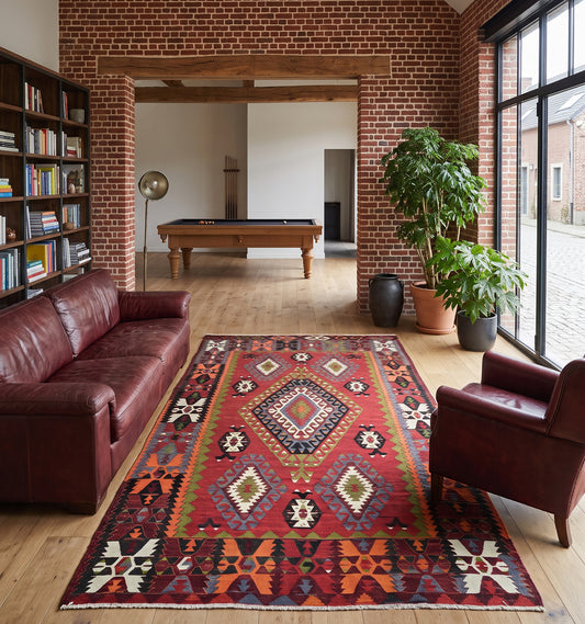 Tapis kilim ancien tissé main en laine par des nomades d’Anatolie, médaillon central losangé rouge et vert olive, posé dans une ferme en briques près de Lille face à un billard et un canapé en cuir