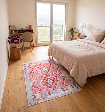 Tapis kilim tissé main au médaillon losangé rose fuchsia et corail, tapis contemporain d’inspiration Anatolie posé dans une chambre à Chambéry face à un bureau en bois et la vue sur les montagnes