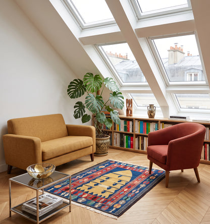 Tapis kilim ancien d'Obruk, tissé main en laine par des nomades d'Anatolie, mihrab safran sur fond bleu profond façon tapis de prière, posé dans un loft parisien face aux verrières et toits de zinc