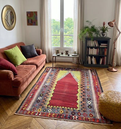 Tapis kilim ancien d'Obruk, tissé main en laine par des nomades d'Anatolie, mihrab rouge et jaune façon tapis de prière, posé dans un salon parisien face à une bibliothèque et un balcon en fer forgé