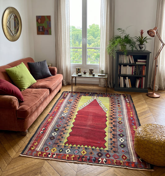 Tapis kilim ancien d'Obruk, tissé main en laine par des nomades d'Anatolie, mihrab rouge et jaune façon tapis de prière, posé dans un salon parisien face à une bibliothèque et un balcon en fer forgé