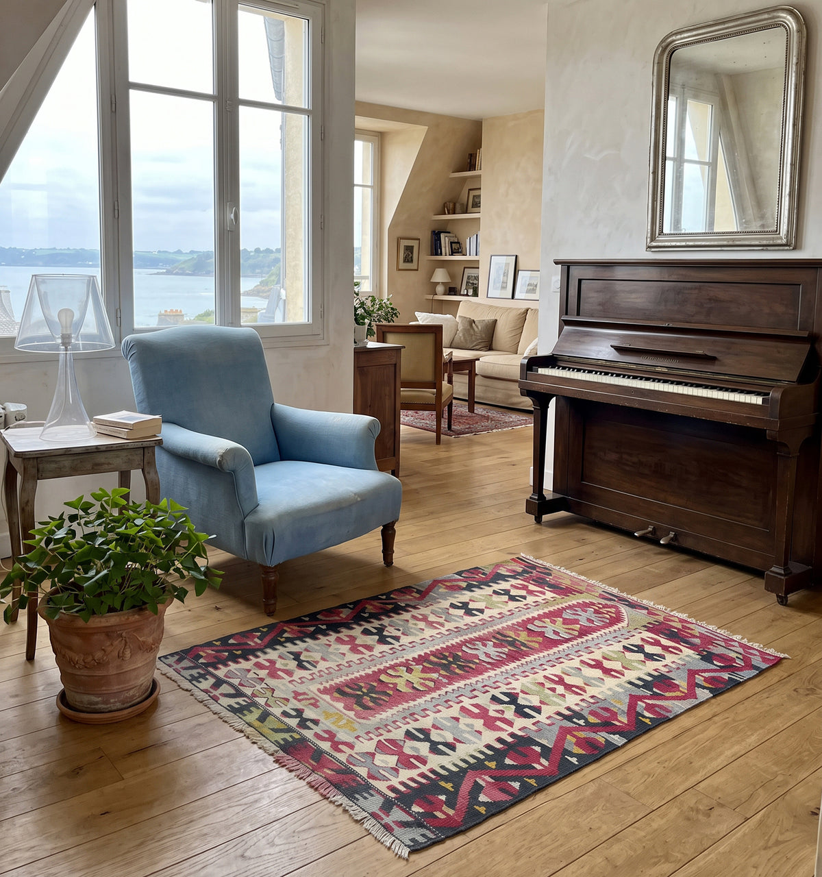 Tapis kilim tissé main aux rayures et croix grenat et vert amande, motifs géométriques hérités des tisserands d'Anatolie, posé dans un salon à Saint Malo face à un piano ancien et la vue sur la baie