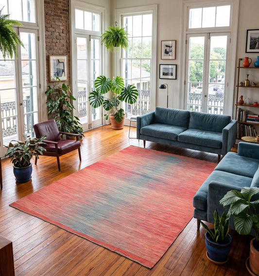 Grand tapis de salon en laine Art Deco avec dégradé horizontal rouge corail et bleu pétrole (298 x 197 cm) mis en situation avec un canapé vieux rose, une table basse en marbre et une grande bibliothèque sombre