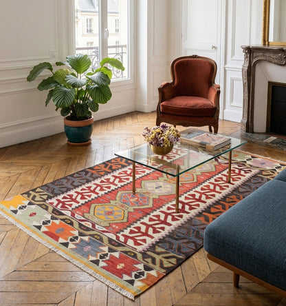 Grand tapis kilim ancien d'Anatolie aux couleurs vibrantes, disposé sur un parquet en chevrons dans un salon élégant. Une pièce maîtresse artisanale qui allie l'authenticité du tissage traditionnel turc à l'esthétique d'un intérieur moderne.