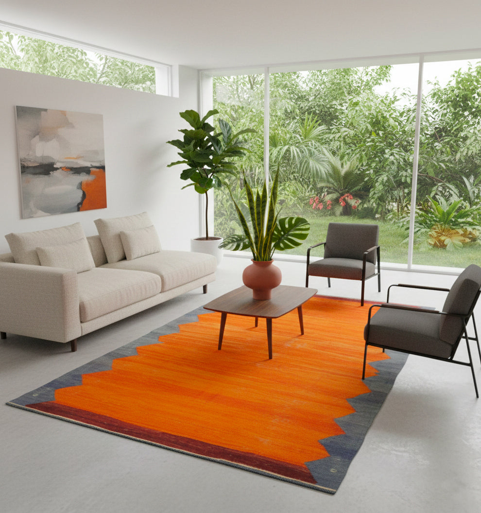 Tapis de salon en laine orange vif avec bordures grises (268 x 142 cm) mis en situation dans un intérieur moderne et lumineux avec canapé blanc et fauteuils gris.