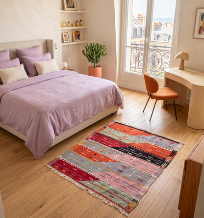 Tapis kilim ancien Sofra, tissé main en laine par des nomades d'Anatolie, rayures géométriques corail et rose poudré, posé dans une chambre à Deauville face à un bureau coiffeuse et une vue sur la mer
