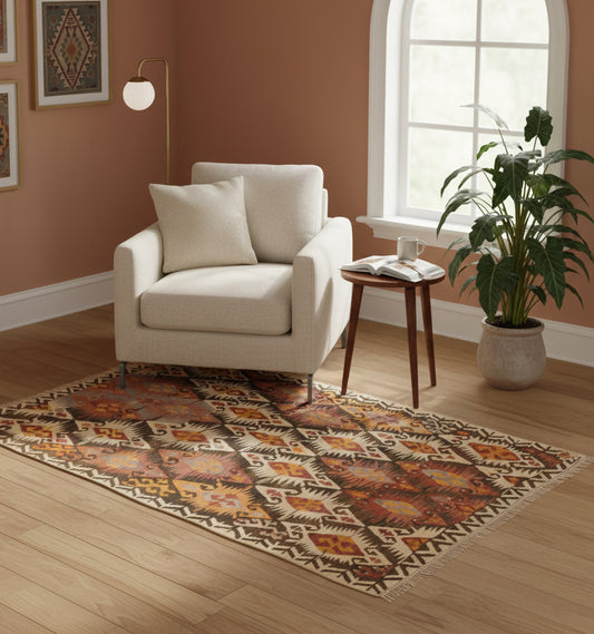 Tapis de salon en laine aux motifs géométriques marron et ocre (188 x 123 cm) mis en situation sous un fauteuil blanc avec une plante verte