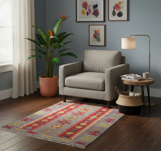 Petit tapis de salon en laine multicolore (140 x 84 cm) placé devant un fauteuil gris dans un coin lecture moderne et lumineux.