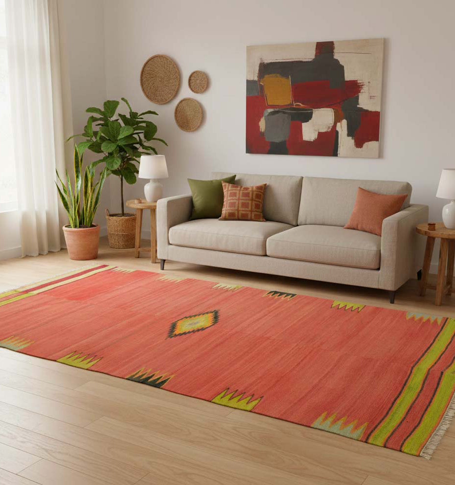Grand tapis de salon en laine couleur corail avec bordures vertes et motif central (264 x 144 cm) mis en situation avec un canapé beige et une décoration murale naturelle