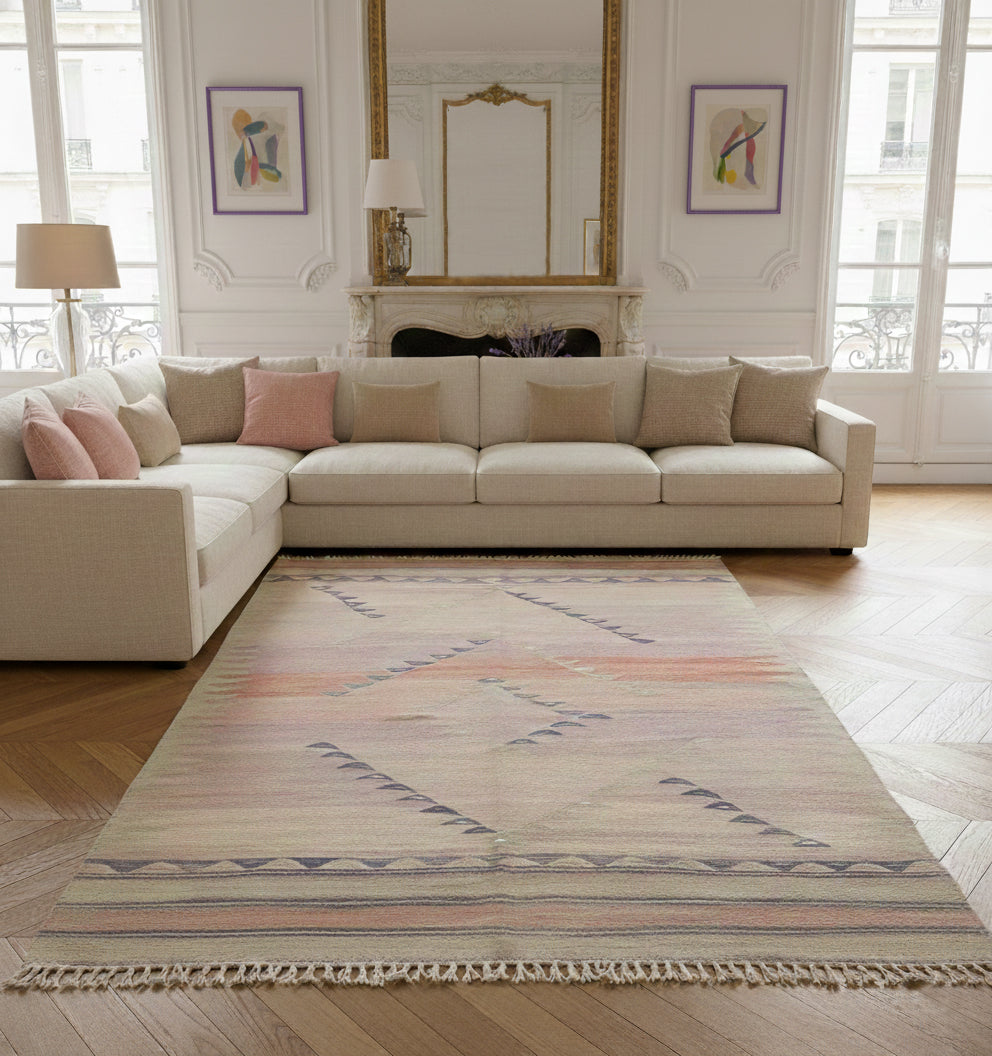 Grand tapis de salon en laine aux tons rose pastel et motifs géométriques gris (210 x 144 cm) mis en situation dans un salon lumineux avec canapé d'angle crème et parquet en chevrons