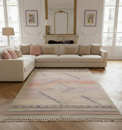 Grand tapis de salon en laine aux tons rose pastel et motifs géométriques gris (210 x 144 cm) mis en situation dans un salon lumineux avec canapé d'angle crème et parquet en chevrons