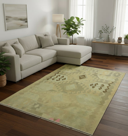 Tapis de salon en laine Kazak vert olive avec motifs tribaux géométriques délavés (290 x 190 cm) mis en situation avec un canapé d'angle crème et un parquet en bois foncé