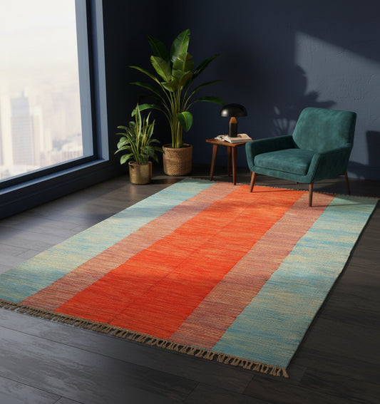 Grand tapis kilim contemporain avec une large bande centrale orange encadrée de bleu (295 x 198 cm) mis en situation dans un salon design avec fauteuil bleu canard, murs sombres, lampe moderne et vue urbaine