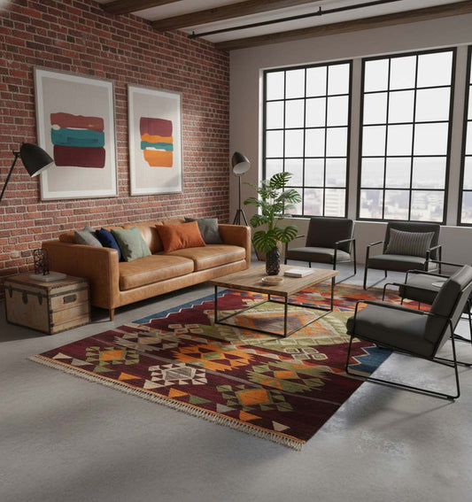 Tapis de salon en laine Koprubasi aux motifs ethniques géométriques colorés (250 x 154 cm) mis en situation dans un salon de style loft industriel avec murs en briques, canapé en cuir camel et larges fenêtres à cadre noir