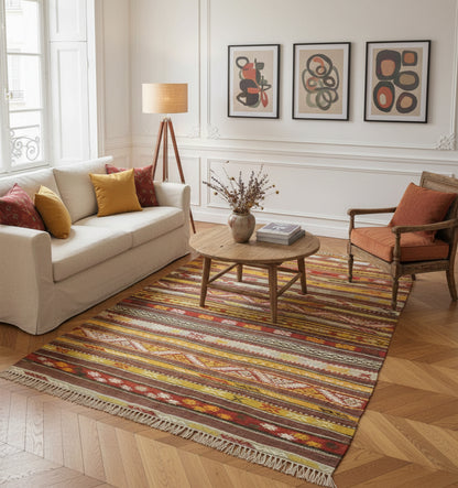Grand tapis de salon en laine aux rayures horizontales ocre et terre cuite (215 x 120 cm) installé sur un parquet en chevrons dans un salon haussmannien avec canapé crème